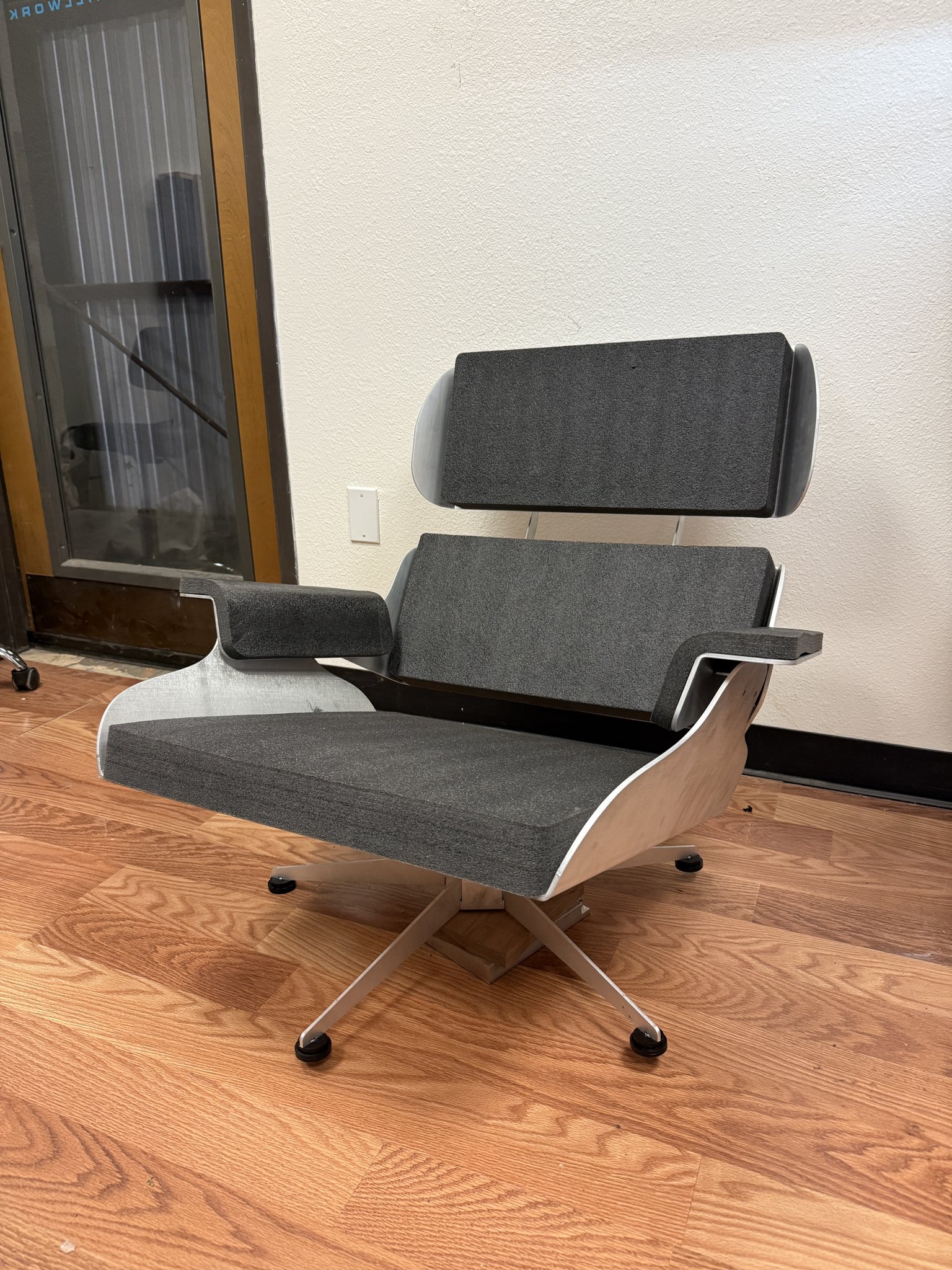 The finished Seames Lounge Chair: bent sheet metal shell with dark grey upholstered cushions on a swivel base