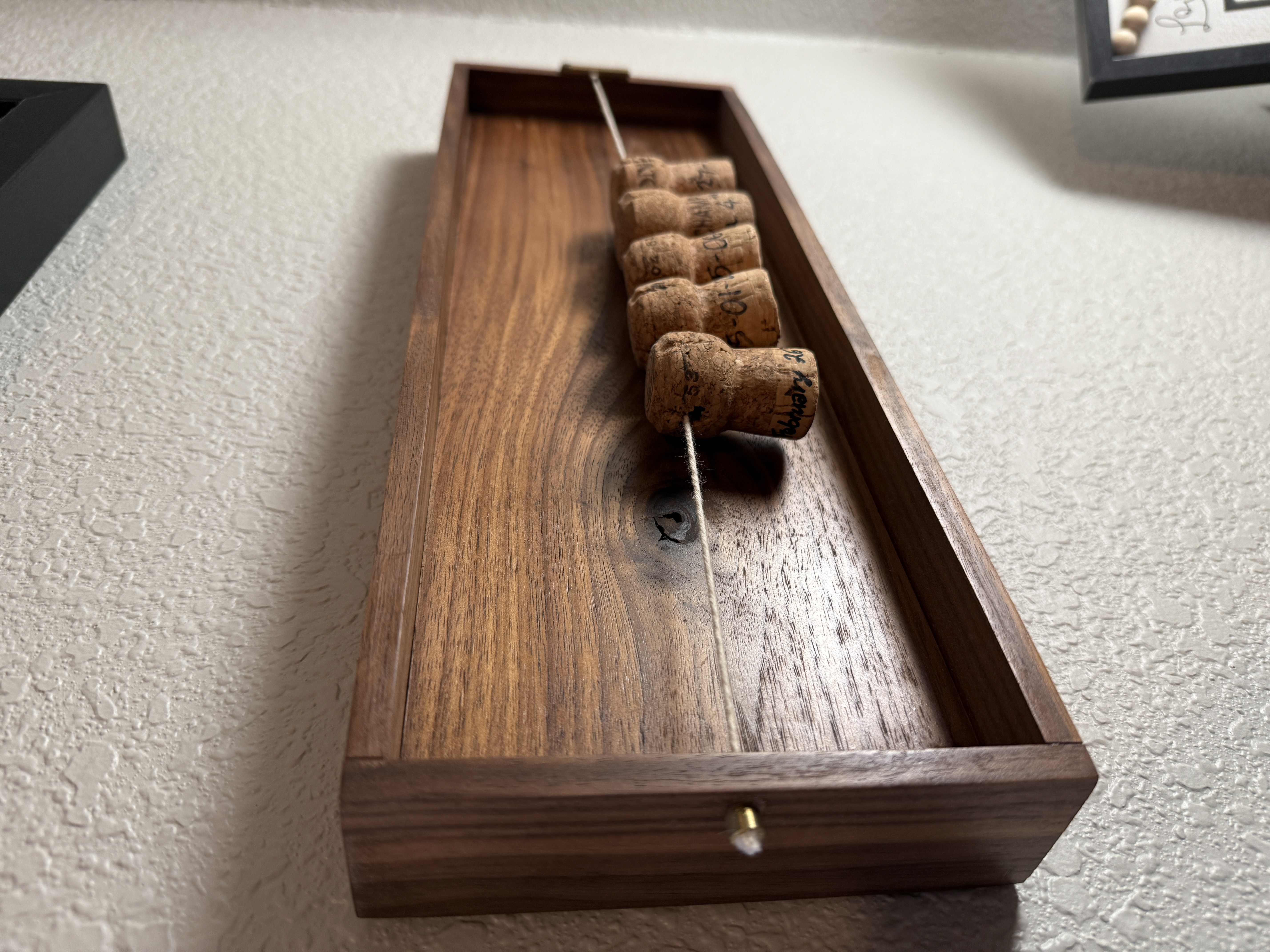 Walnut memory holder with champagne corks strung along a line inside the tray